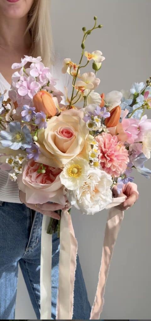 Soft pastel-colored flower bouquet with roses, peonies, orchids, and daisies.