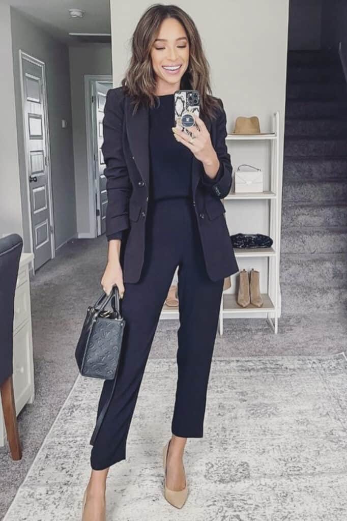 Stylish woman in black suit taking mirror selfie in modern home, elegant fashion, professional attire.