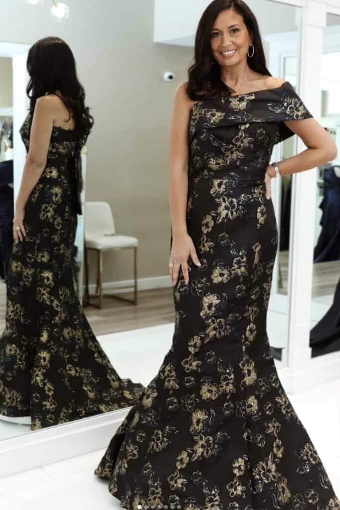 Elegant woman in black and gold floral evening gown posing indoors.