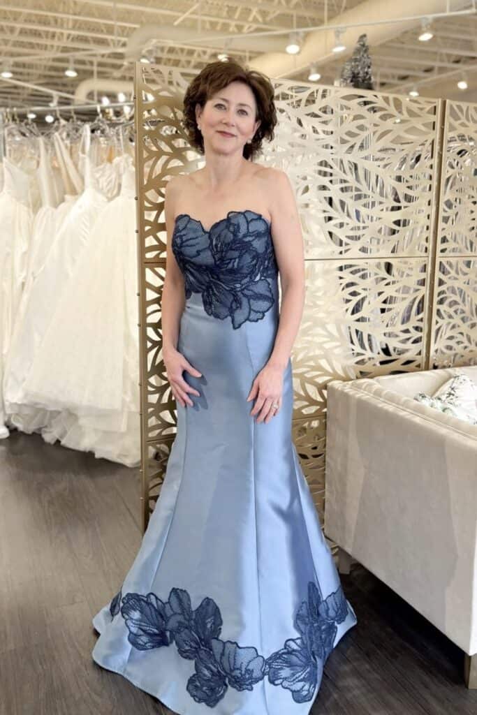 Elegant blue evening gown with floral lace details at Confetti & Roses.