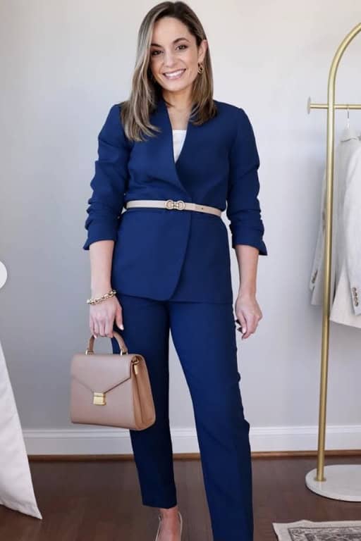 Elegant woman in blue suit with beige handbag and gold accessories.