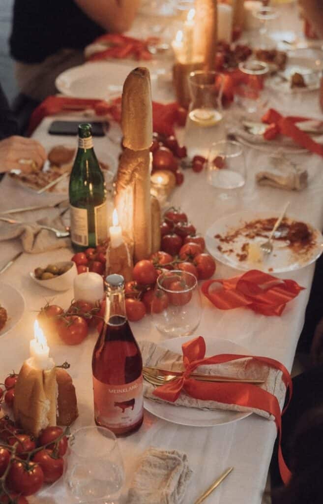 Rustic dinner table with tomatoes, candles, wine and bread for festive celebration.