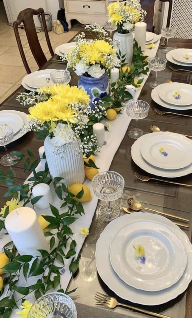 Bright yellow and white floral table centerpiece with candles and greenery for elegant event decor.