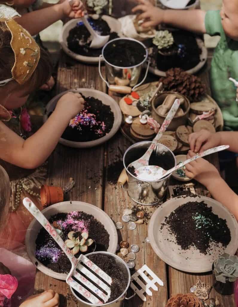 Colorful children's craft activity with soil, glitter, and decorations on a rustic wooden table.