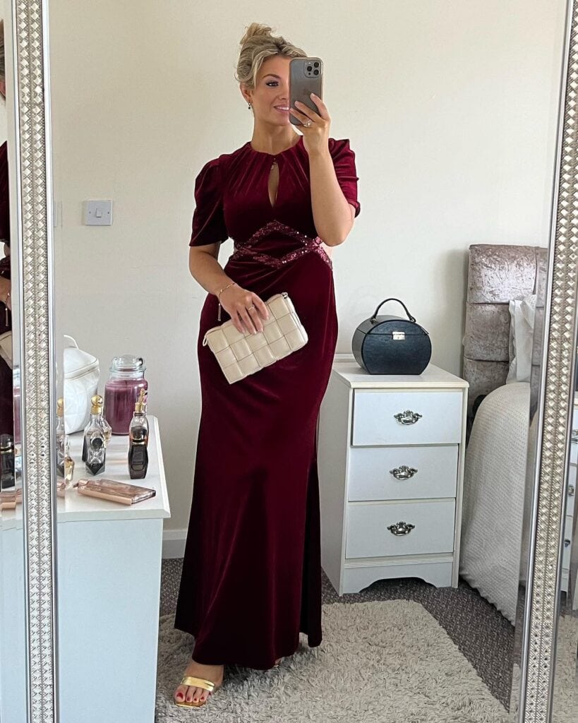 Elegant woman in burgundy gown taking mirror selfie for special occasion.