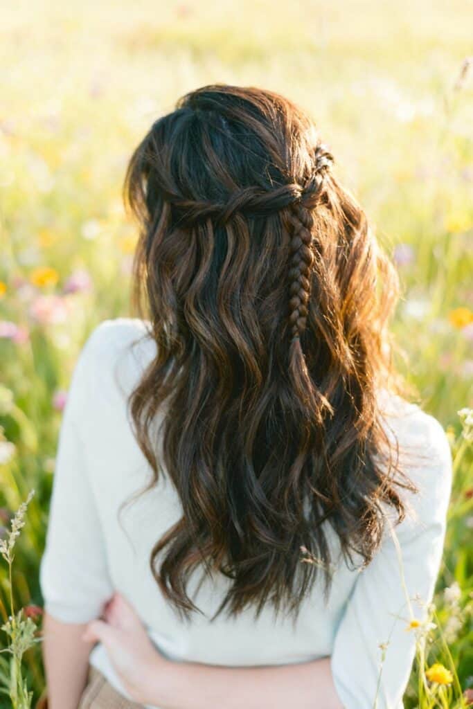 Braid hairstyle with loose waves on woman in a floral field during golden hour.