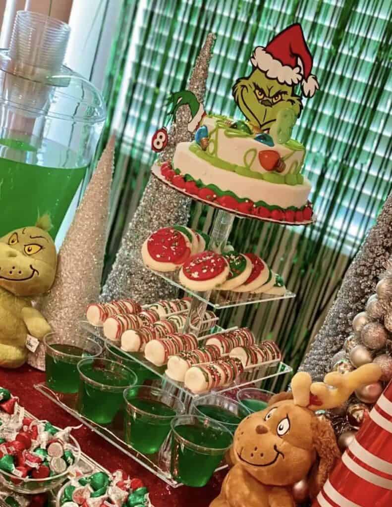 Colorful Dr. Seuss-themed Christmas cake with Grinch topper and holiday treats.