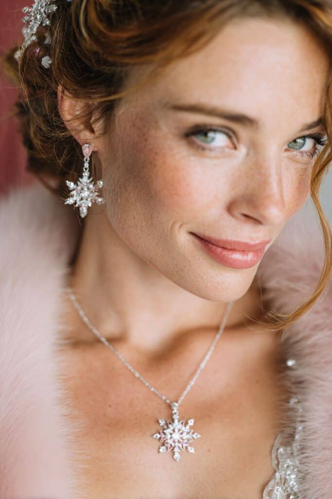 Dazzling snowflake-shaped diamond jewelry worn by a smiling woman with red hair and blue eyes.