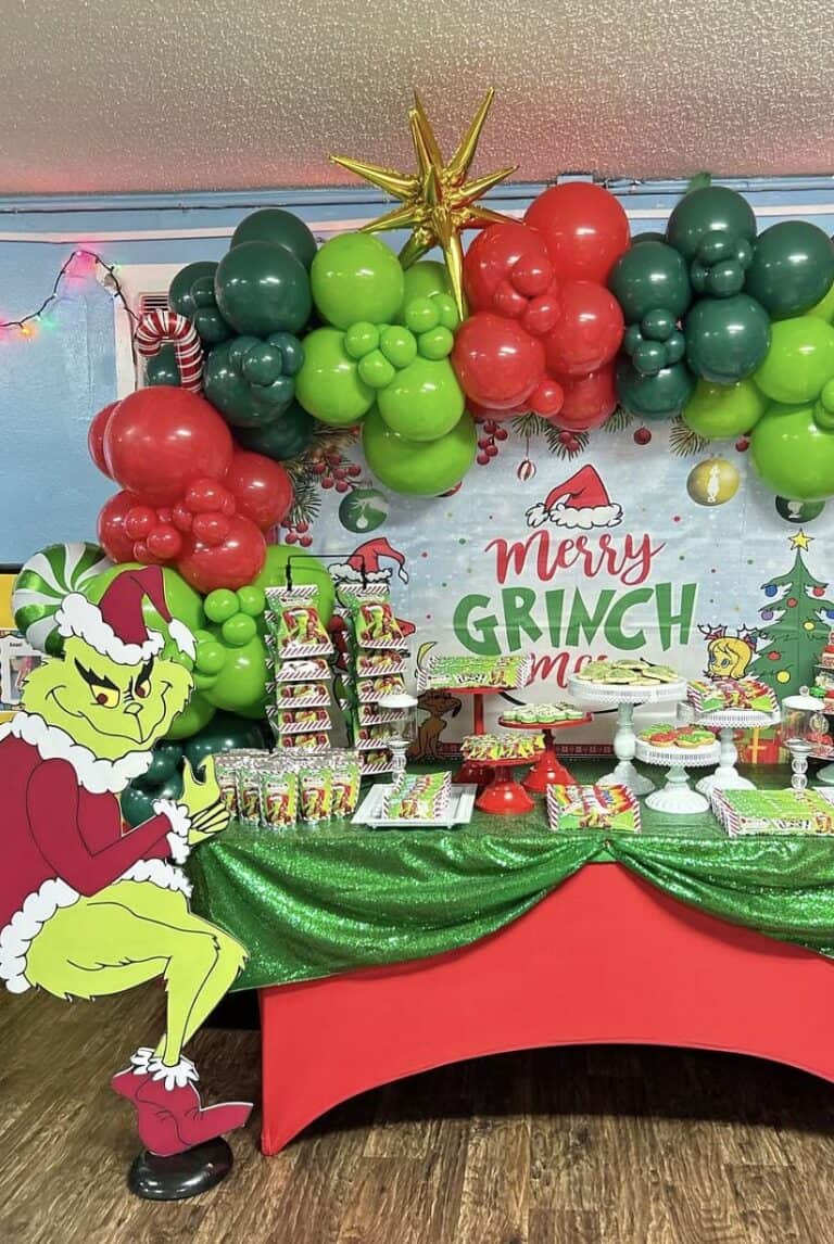 Colorful Grinch-themed balloon decoration with holiday treats and festive backdrop.