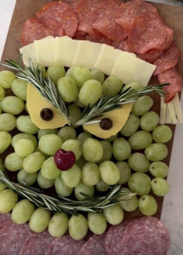Grapes and cheese platter with salami and rosemary garnish.