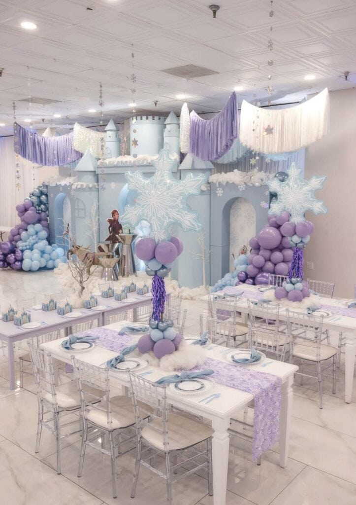 Whimsical winter-themed party decoration with castle, snowflakes, balloons, and pastel colors.