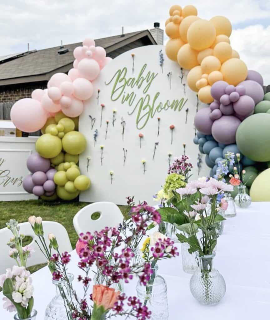 Colorful balloon arch with "Baby in Bloom" sign at outdoor baby shower.