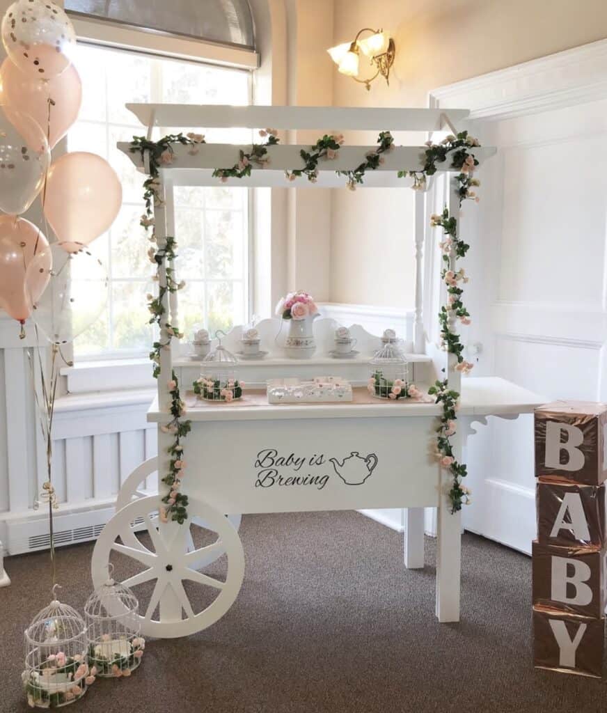 Baby shower tea party décor with pink floral accents and "Baby is Brewing" sign.