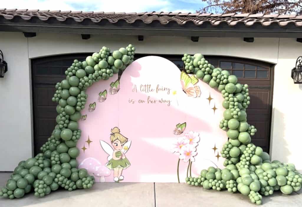 Delicate fairy-themed balloon arch with pink backdrop and fairy illustration.
