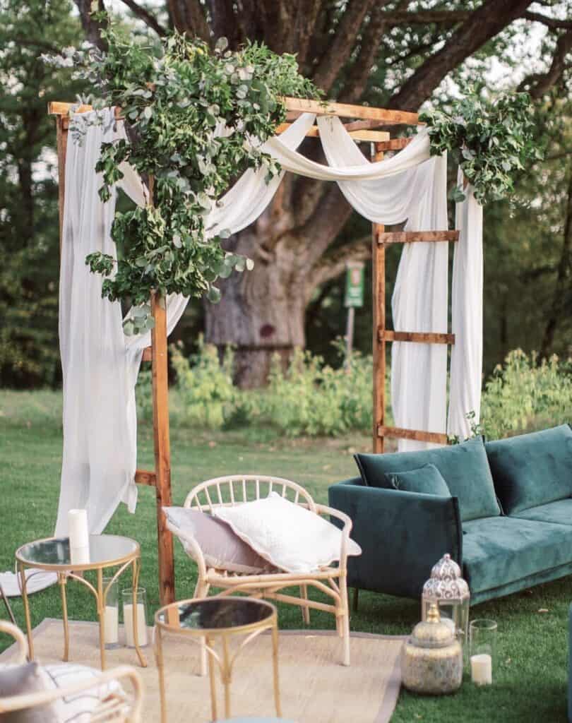 Elegant outdoor wedding arch with greenery, white drapery, and floral accents for boho wedding decor.