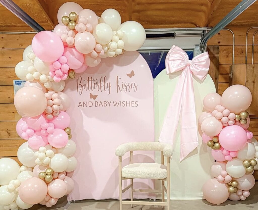 Butterfly kisses baby shower backdrop with pink, white, and gold balloons and a bow.