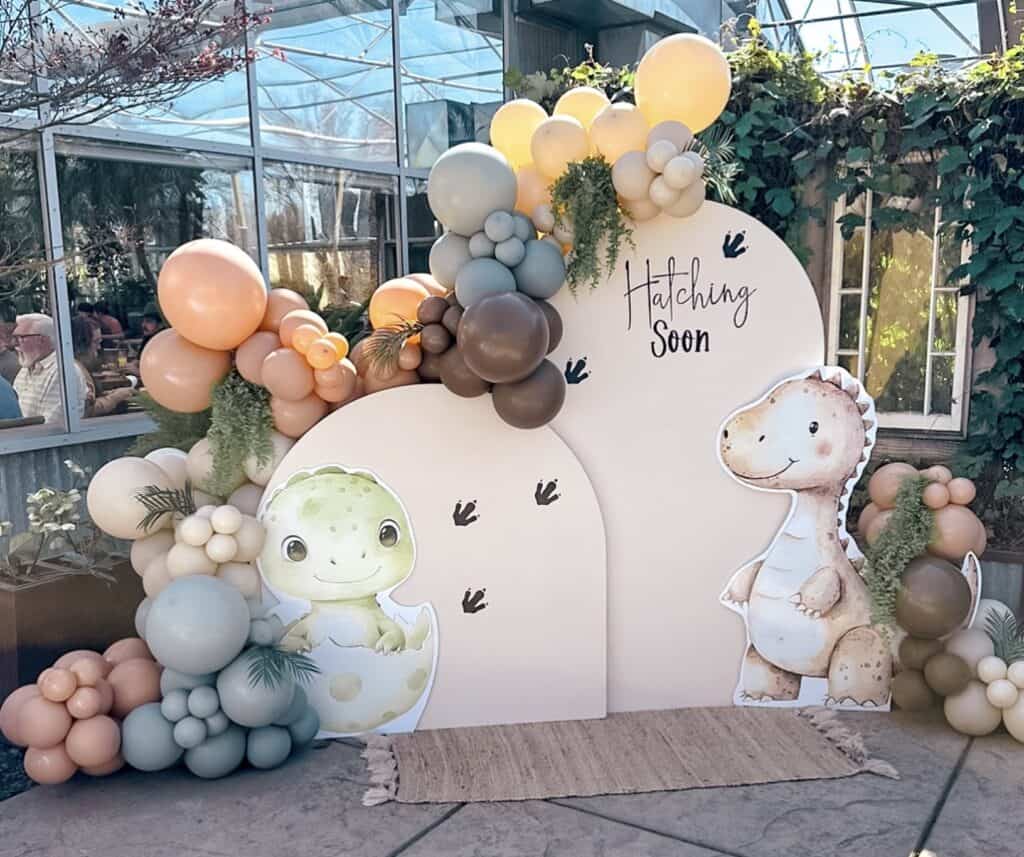 Colorful balloon arch with cartoon dinosaur and hatching soon sign, perfect for baby shower.