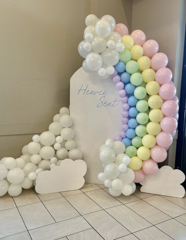 Colorful balloon arch with pastel pink, yellow, blue, and green balloons and cloud-shaped accents.