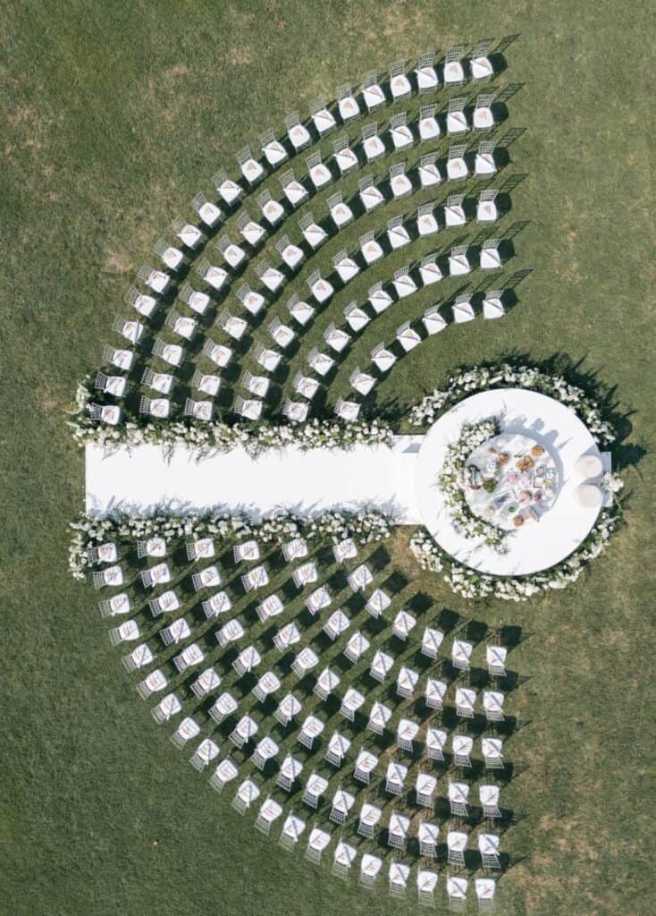 Elegant outdoor wedding setup with white chairs and floral aisle decorations.