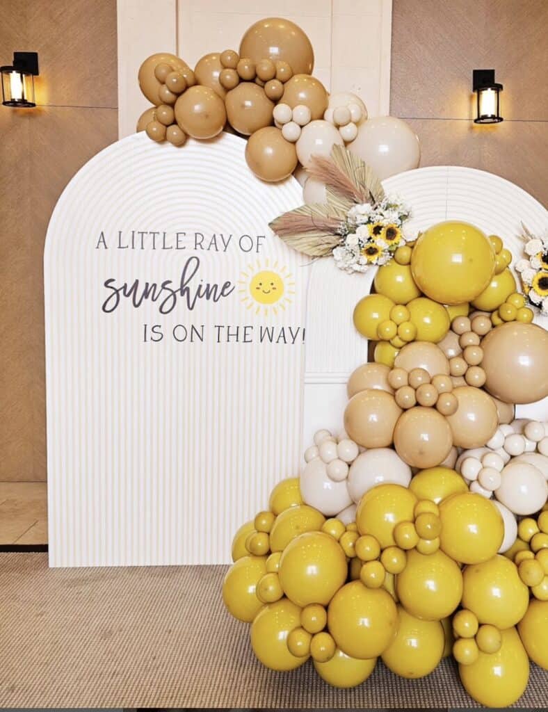 Bright yellow and beige balloon arch with floral accents at event decor.