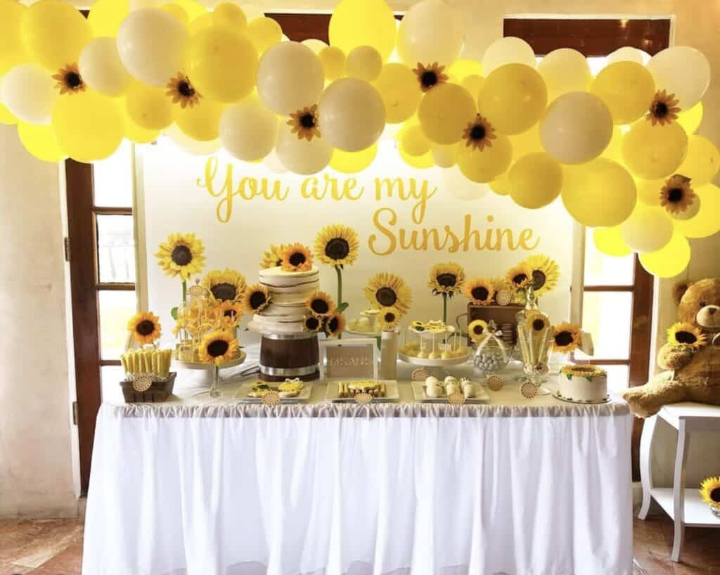 Bright sunflower-themed birthday party with yellow and white balloons and dessert table.