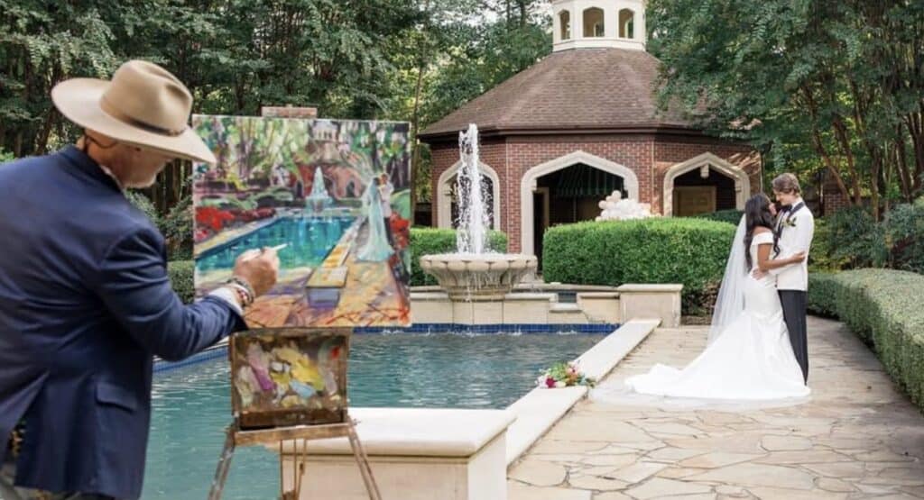 Elegant wedding couple at outdoor ceremony with artist painting in the background.