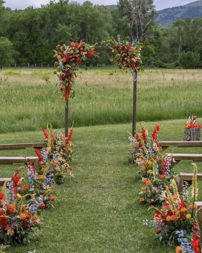 Colorful outdoor wedding arch decorated with vibrant flowers in a scenic green field.