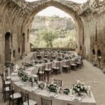 Elegant wedding reception decorated with floral centerpieces under ancient stone archway.
