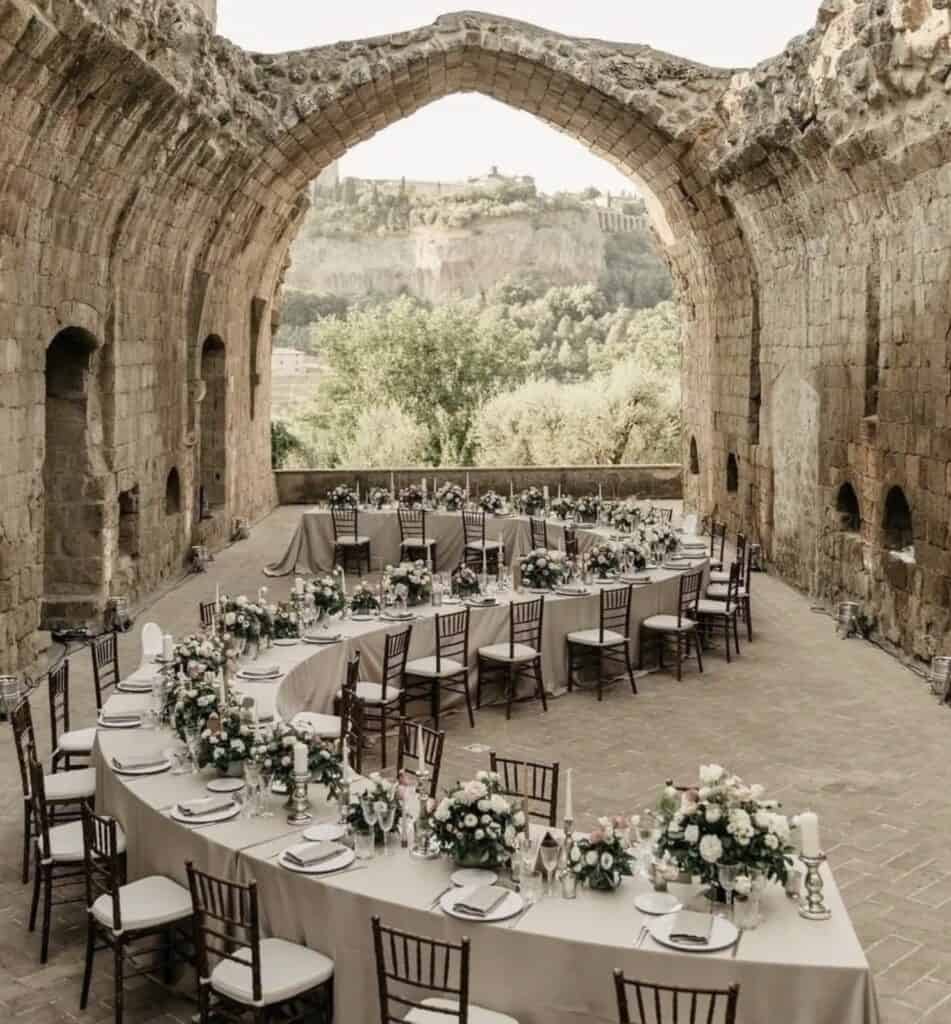 Elegant wedding reception decorated with floral centerpieces under ancient stone archway.