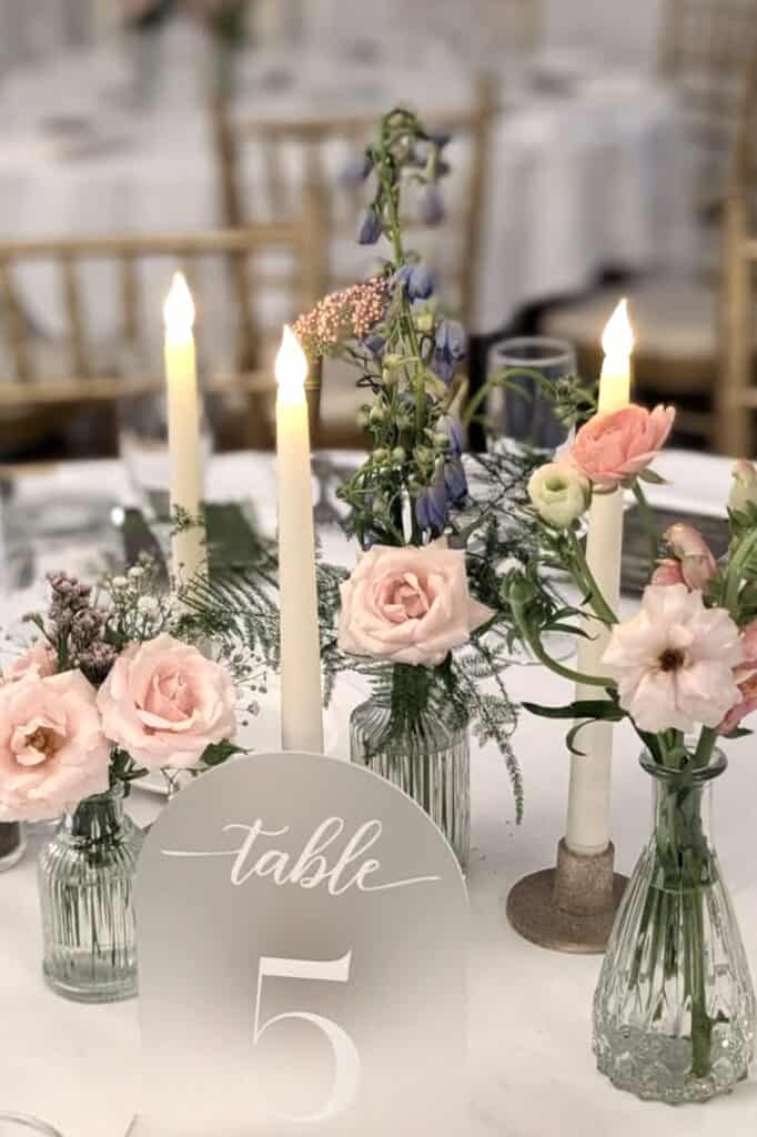 Elegant floral centerpiece with pink roses and candles at wedding reception.