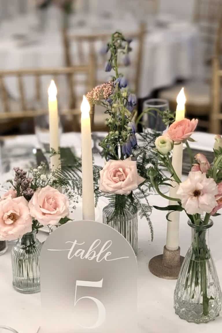 Elegant floral centerpiece with pink roses and candles at wedding reception.