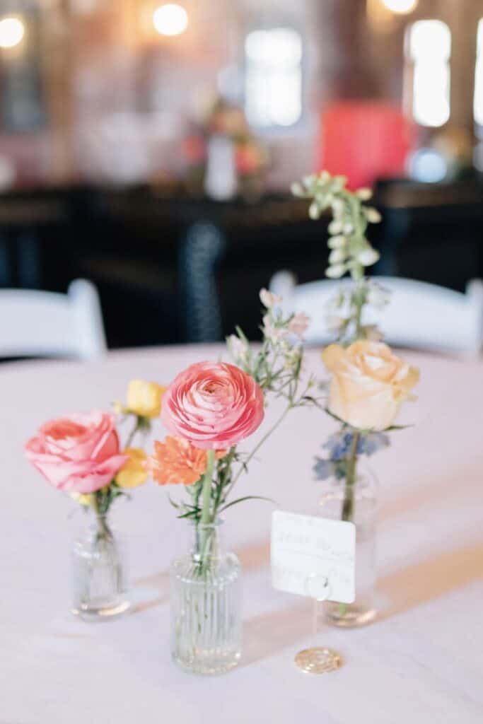 Elegant floral centerpiece with pastel roses and ranunculus in glass vases at event table.