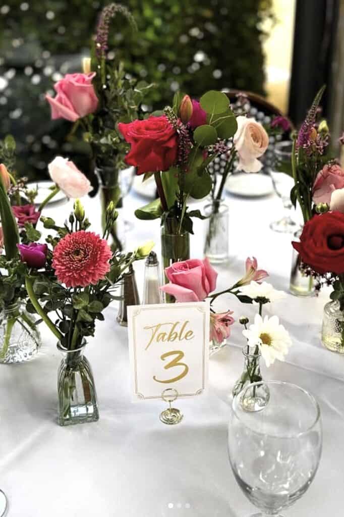 Elegant floral centerpiece with pink roses, daisies, and greenery for wedding reception.