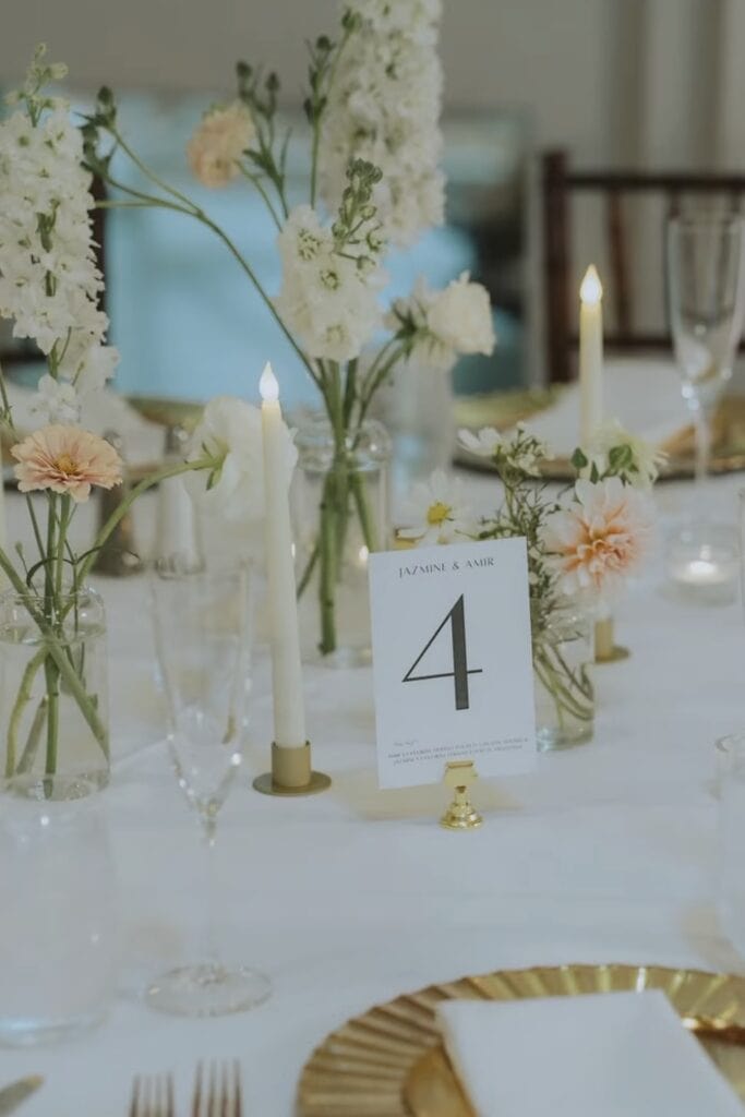 Elegant wedding table centerpiece with white and blush flowers, candlelight, and table number sign.