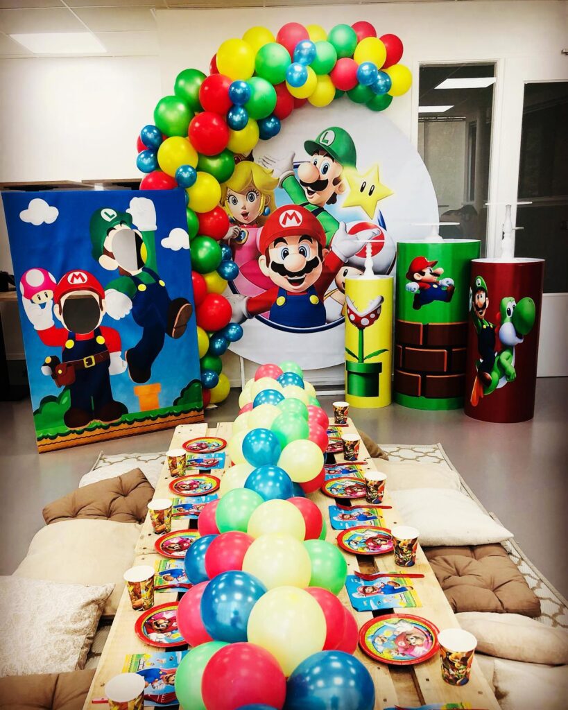 Super Mario themed birthday party decoration with balloons, character cutouts, and table setup.