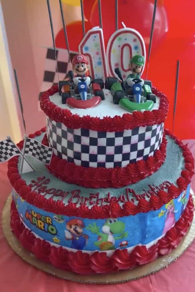 Mario Kart themed birthday cake with Mario and Luigi figurines, checkered pattern, and "Happy Birthd.