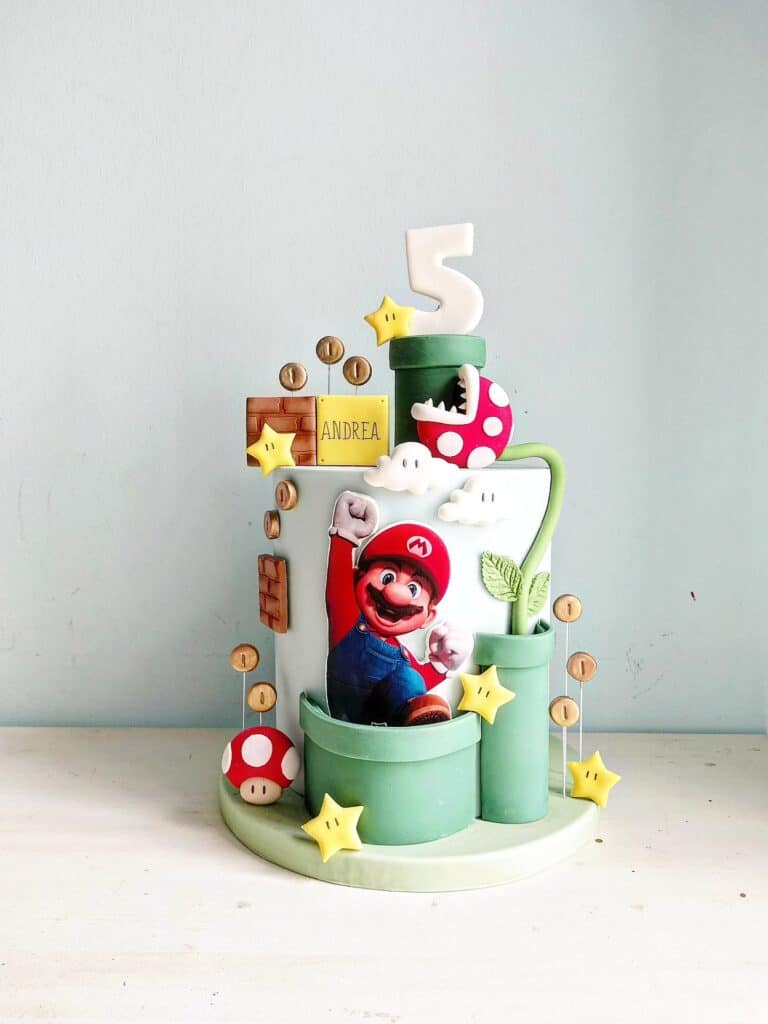A colorful Super Mario-themed birthday cake with Mario figurine, mushrooms, stars, and number five t.