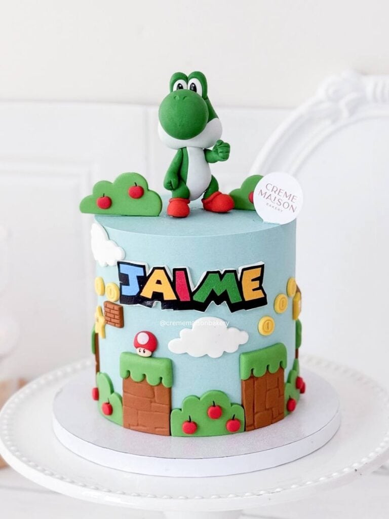 A colorful Super Mario-themed birthday cake with Yoshi figurine, mushrooms, clouds, and coins.
