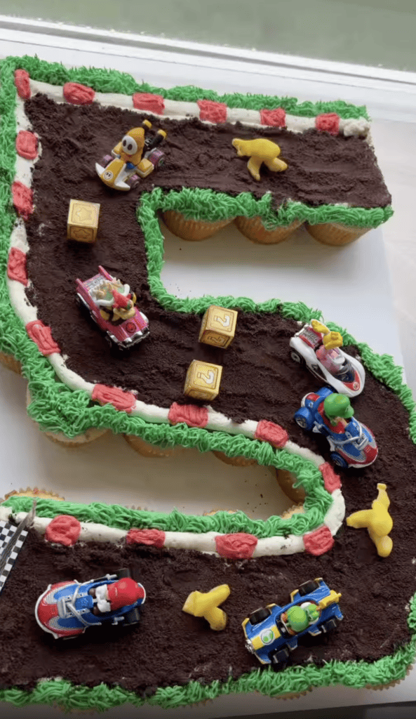 A colorful Super Mario-themed birthday cake with toy cars and characters, perfect for kids' parties.