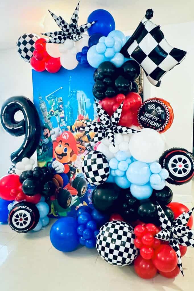 A colorful Mario Kart-themed balloon arrangement with checkered flags, racing wheels, and birthday d.