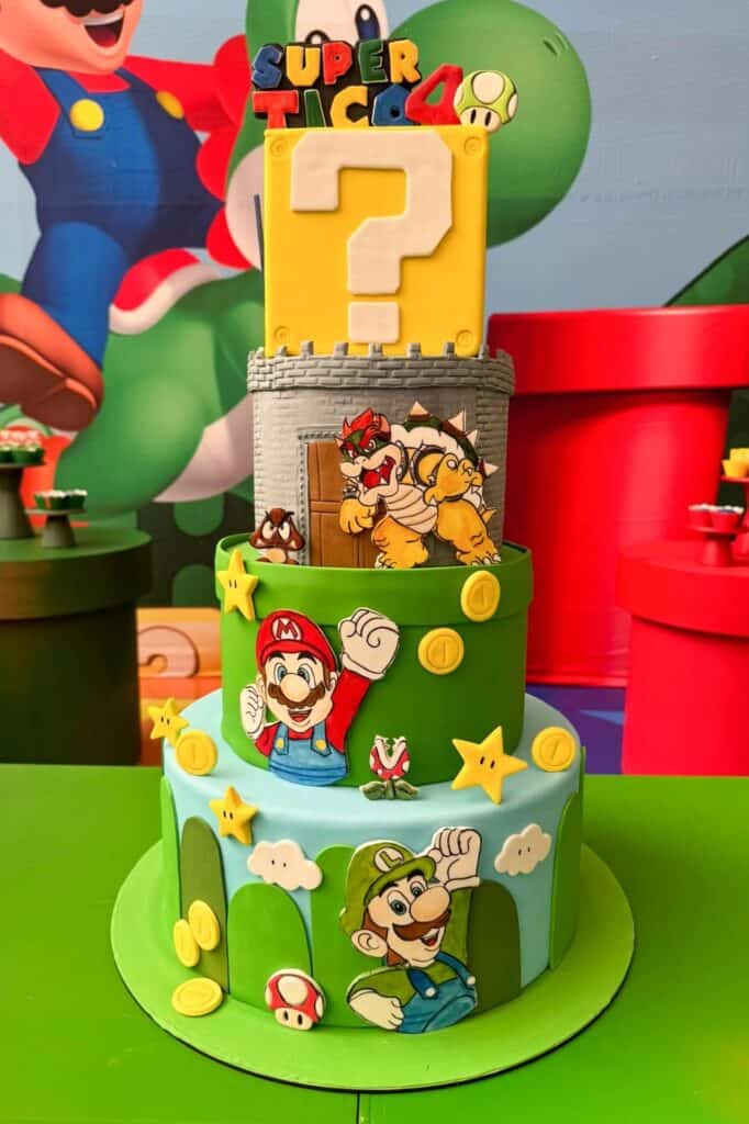 A colorful Super Mario-themed birthday cake with Mario, Luigi, and Bowser figurines, featuring quest.