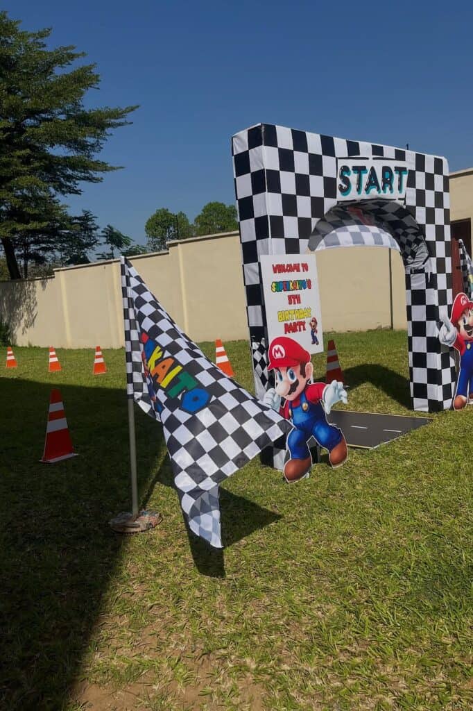 Mario Kart themed outdoor race start line with checkered flags, inflatable characters, and race cone.