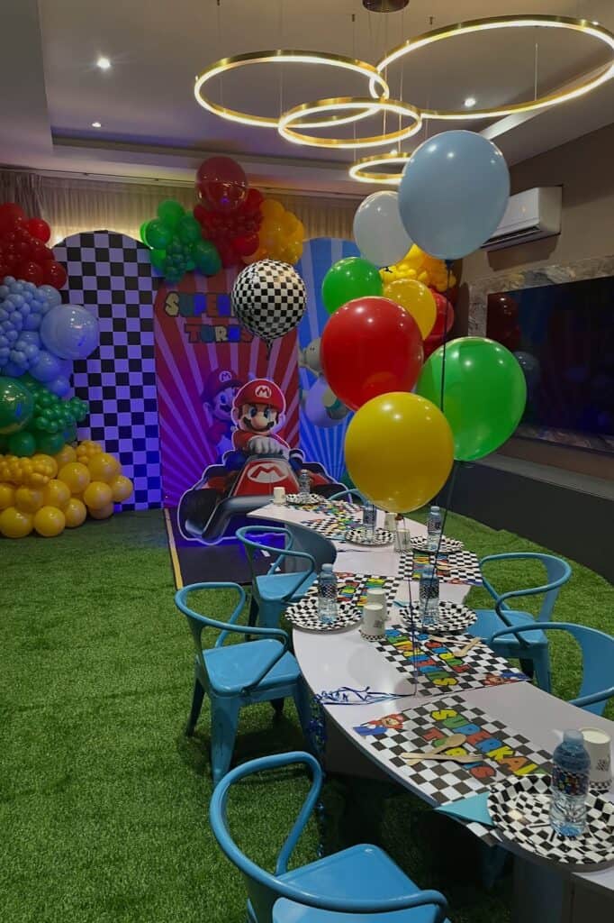 A colorful Mario Kart-themed birthday party setup with balloons, checkered tableware, and themed dec.