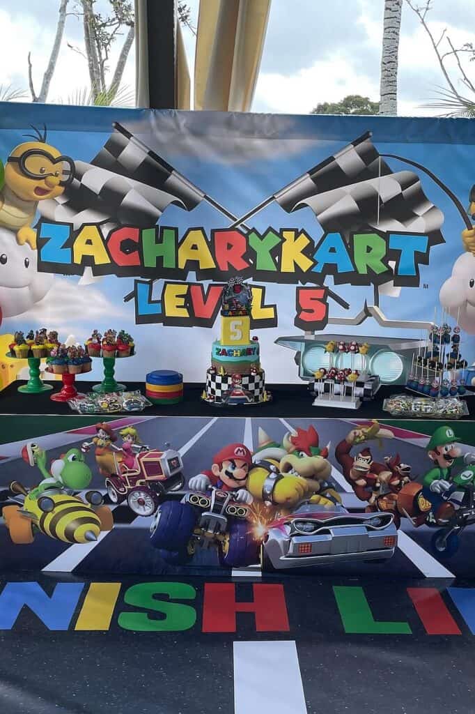 A colorful Mario Kart themed birthday party setup with decorations, cake, and toy cars for a child's.