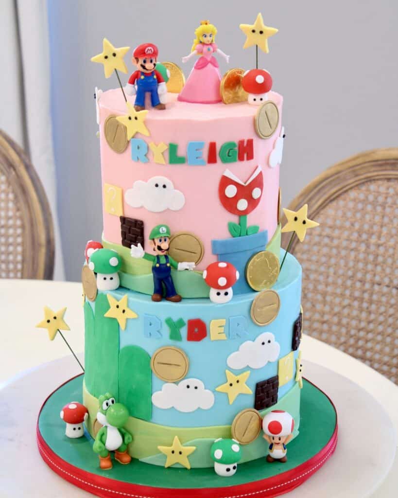 A colorful Super Mario-themed birthday cake with Mario, Princess Peach, Yoshi, and various Mario ico.