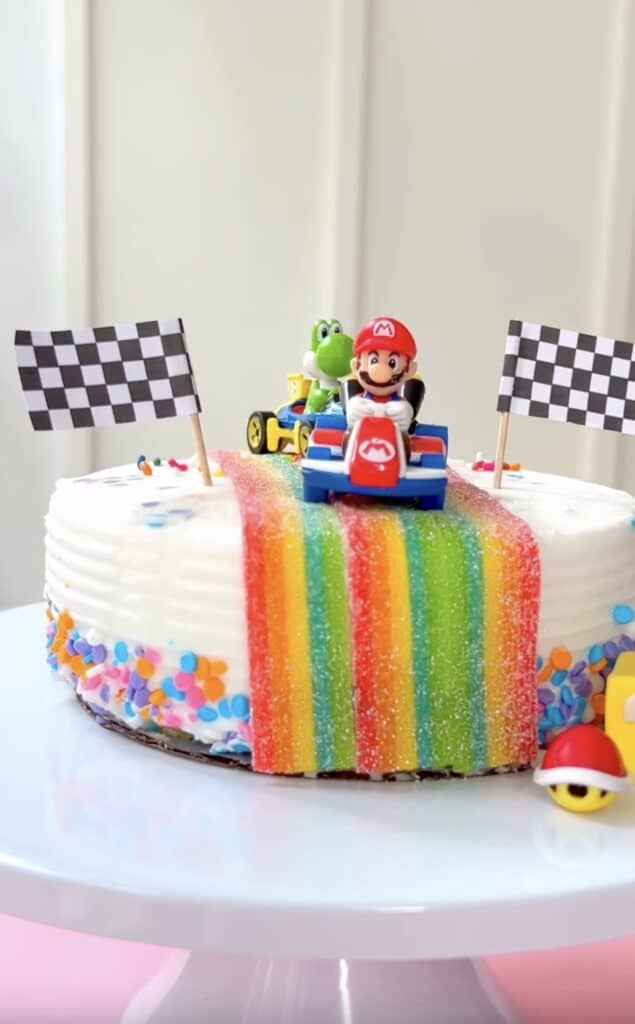 A colorful Mario-themed birthday cake with rainbow sprinkles and Mario and Yoshi figurines.