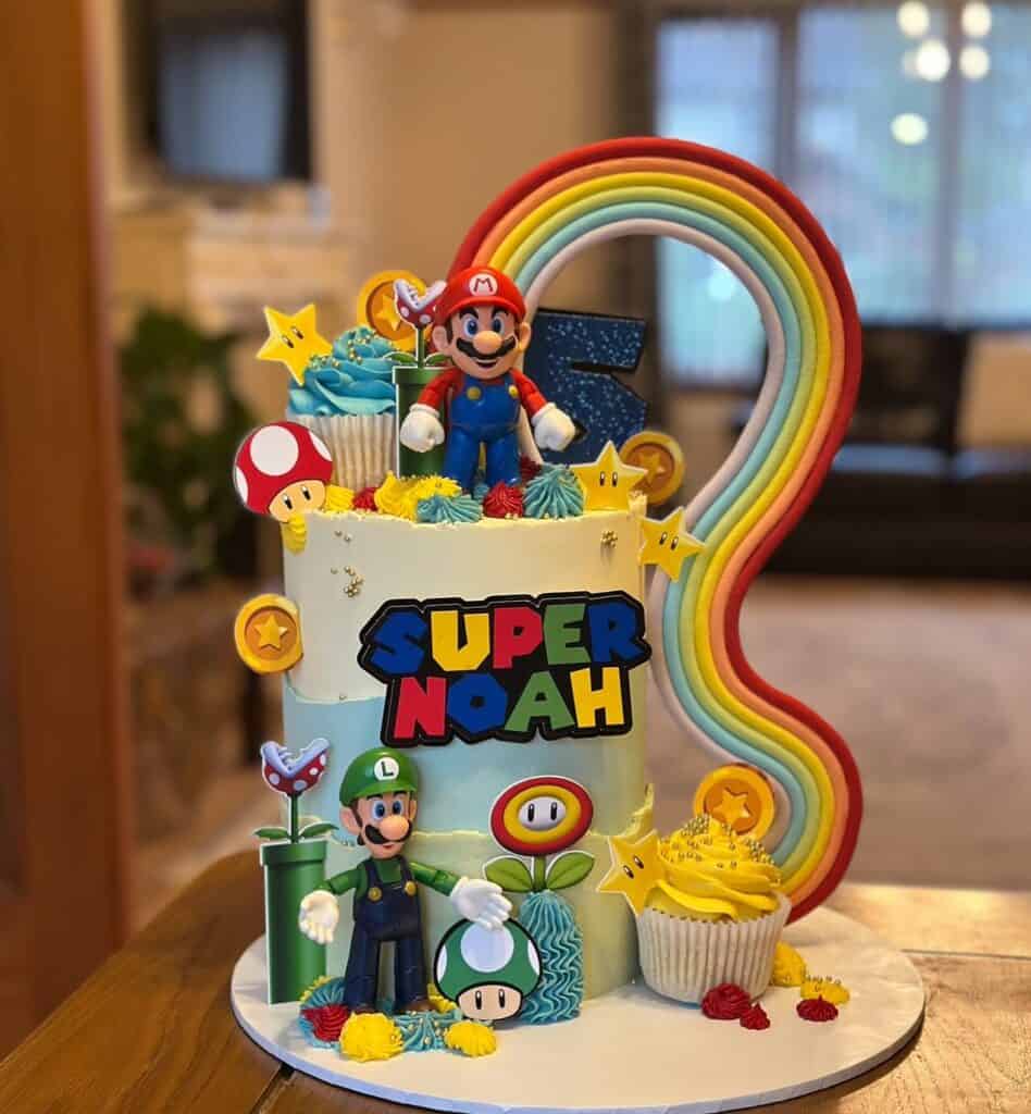 Super Mario-themed birthday cake with rainbow decoration and character figurines for a 5th birthday.