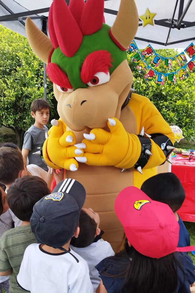 A colorful Bowser mascot entertaining children at a birthday party with festive decorations and outd.
