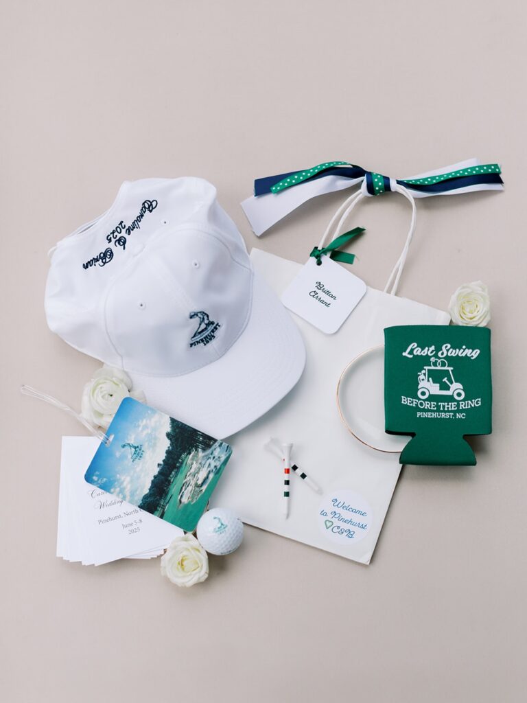 A white golf cap with embroidered logo, golf ball, and wedding-themed accessories on a neutral backg.