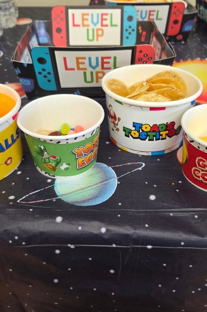 LEGO-themed party cups with snacks and Nintendo Switch "Level Up" decorations for Yoshi birthday cel.